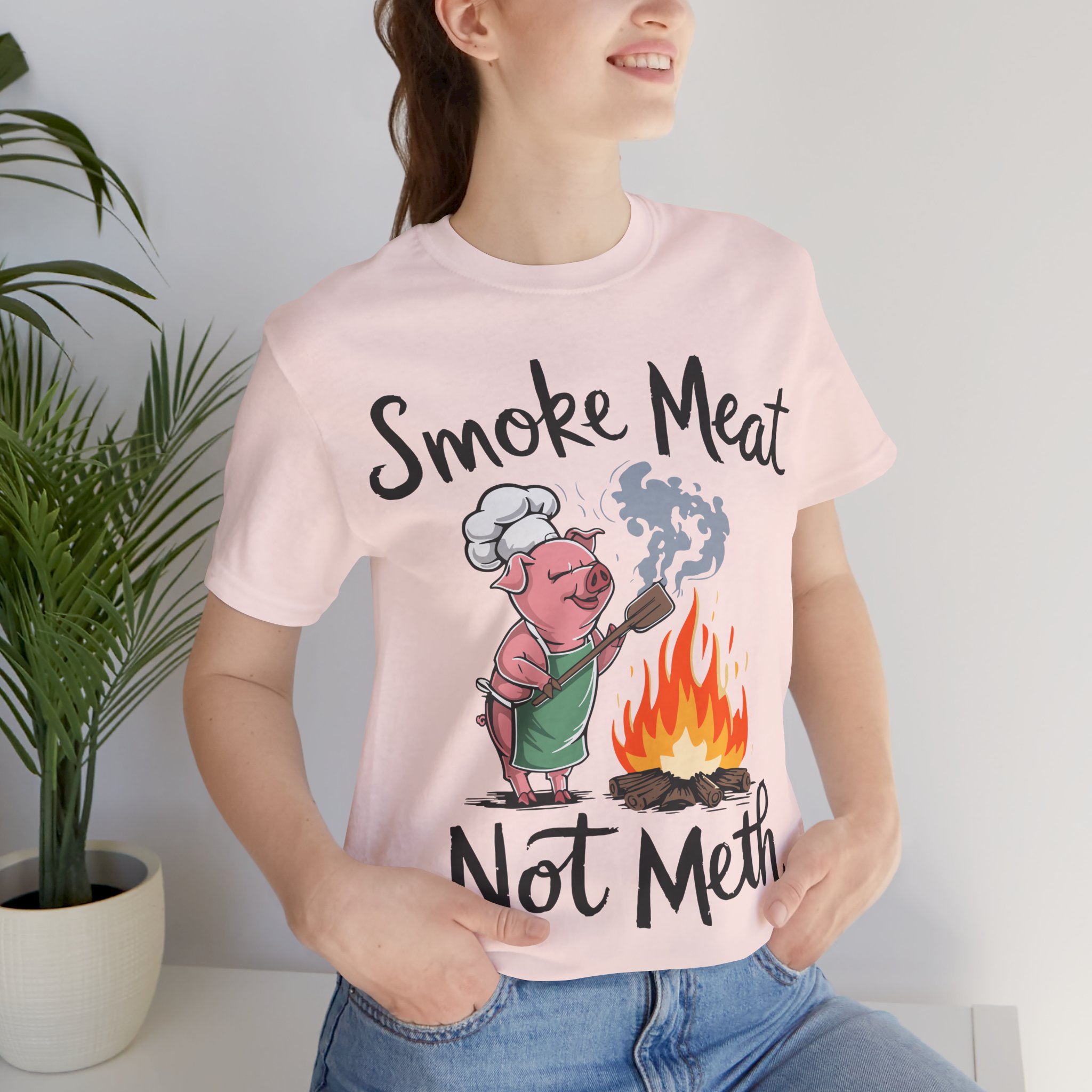 A pink Bella and Canvas t-shirt. A lightweight, comfortable jersey short-sleeve t-shirt with a witty BBQ-inspired design, ideal for summer gatherings, cookouts, or as a fun gift for meat-smoking aficionados.